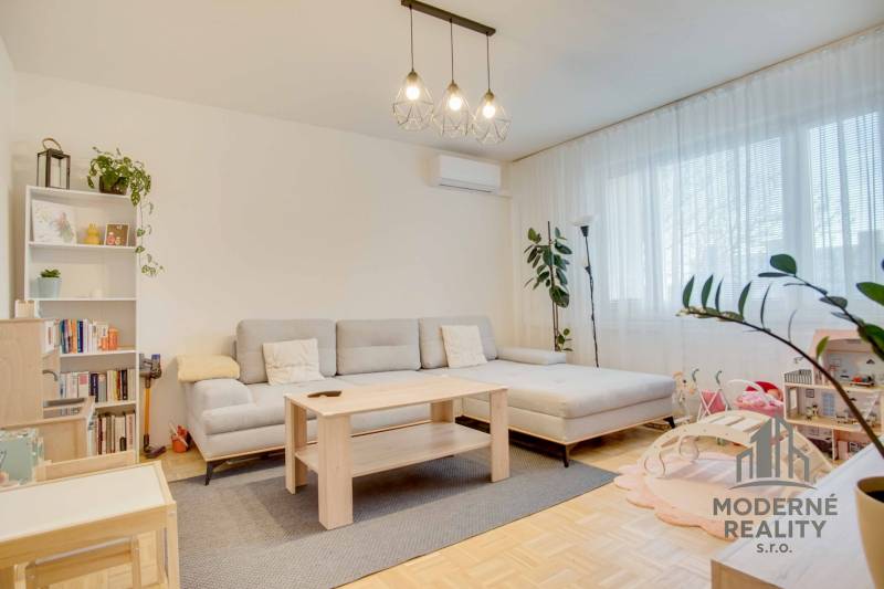 A bright living room with a sofa and wood-patterned flooring in a three-room apartment.