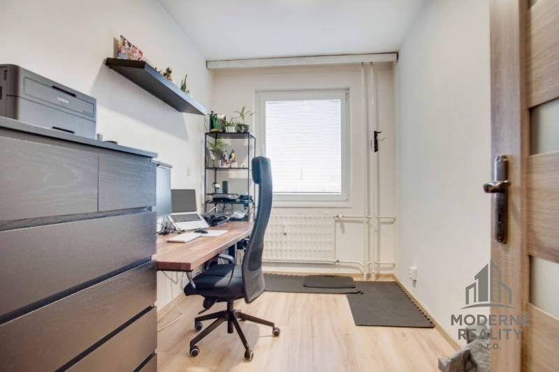 Home office with a desk, chair, and shelf in a 3-room apartment with wood-patterned flooring.