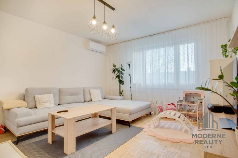 A bright living room with a sofa, children's toys, and a wooden decor floor in a 3-room apartment.
