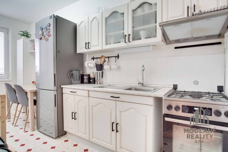 Kitchen in a 3-room apartment with white cabinets, a stove, and a large refrigerator.