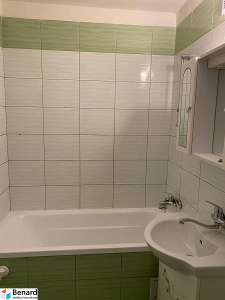 A bathroom in a 3-room apartment with green tiles and a bathtub next to the sink.