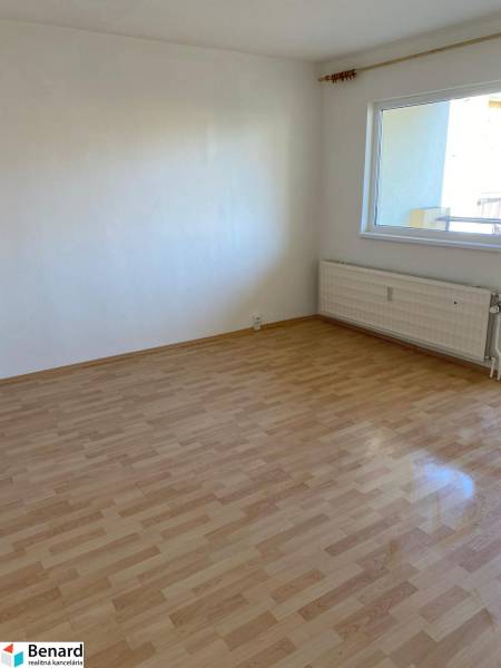 A room with a wooden decor floor in a 3-room apartment, light wall, radiator.