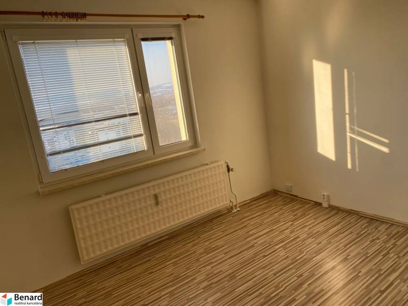 A room with a large window and a wooden decor floor in a 3-room apartment.
