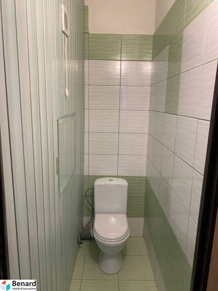 A toilet in a 3-room apartment with tiles in green and white tones.