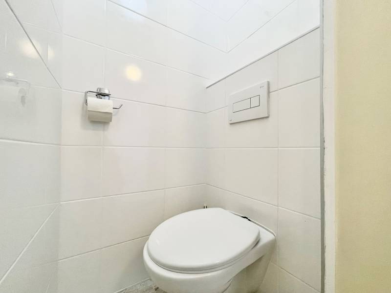 A toilet with white tiles and toilet paper in a studio apartment.