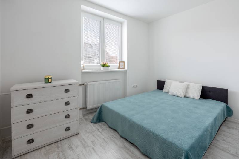 A bright bedroom with a double bed, a dresser, and a wooden decor floor in a two-room apartment.
