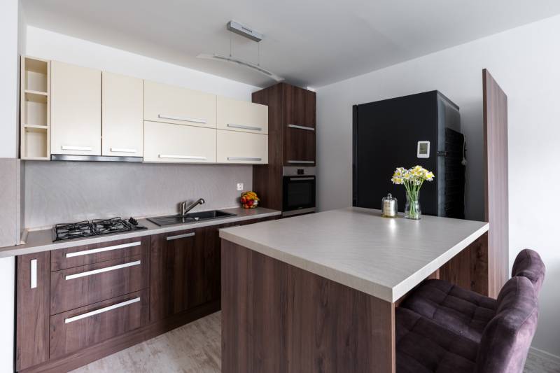 A kitchen in a 2-room apartment with a wooden decor floor, a bar counter, and modern equipment.