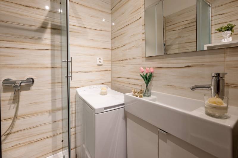 A bathroom in a 2-room apartment with a washing machine, shower, and cozy decoration.