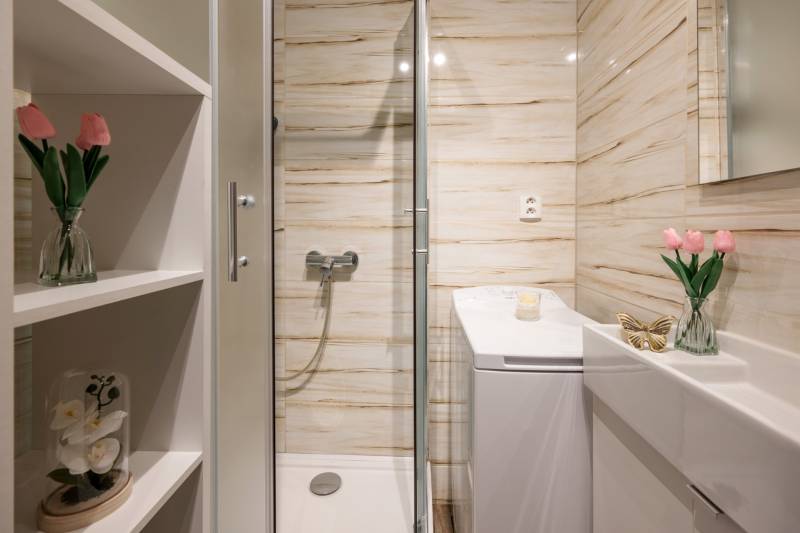 Bathroom with flowers, shower, sink, and mirror in a 2-room apartment.