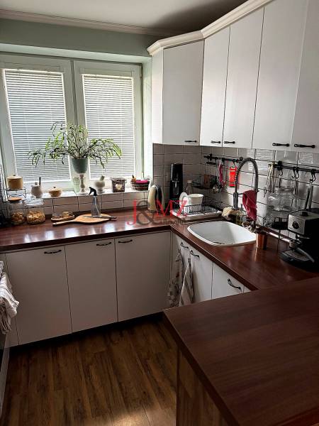 The kitchen of a two-room apartment with a wooden decor floor and white cabinets.