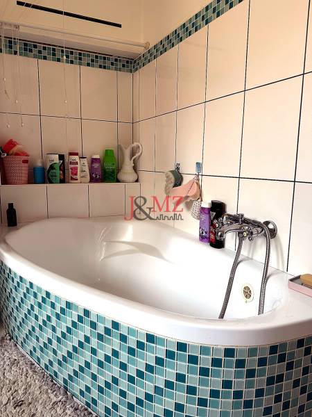 A bathroom with a corner bathtub and blue-white tiles in a 2-room apartment.