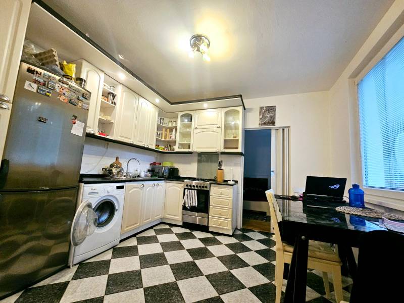 A kitchen in a 3-room apartment with tiles, equipped with appliances and a dining table.