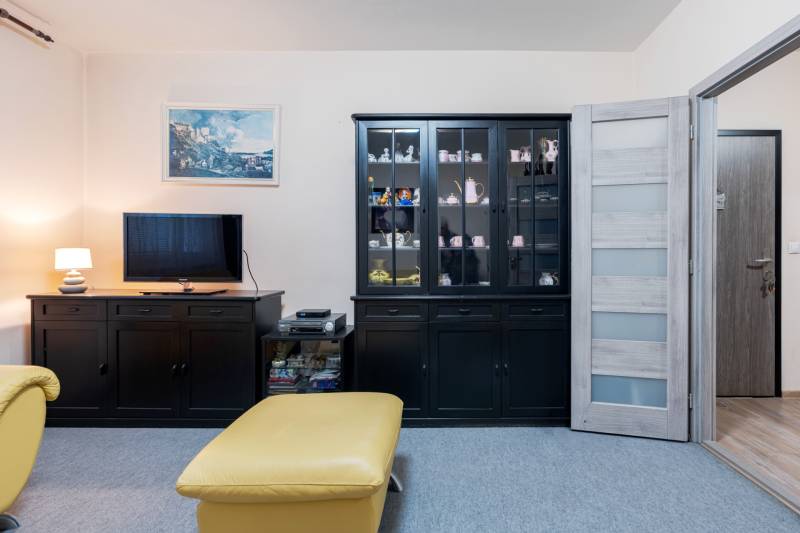 Living room in a 4-room apartment with dark furniture, a television, and a display cabinet.
