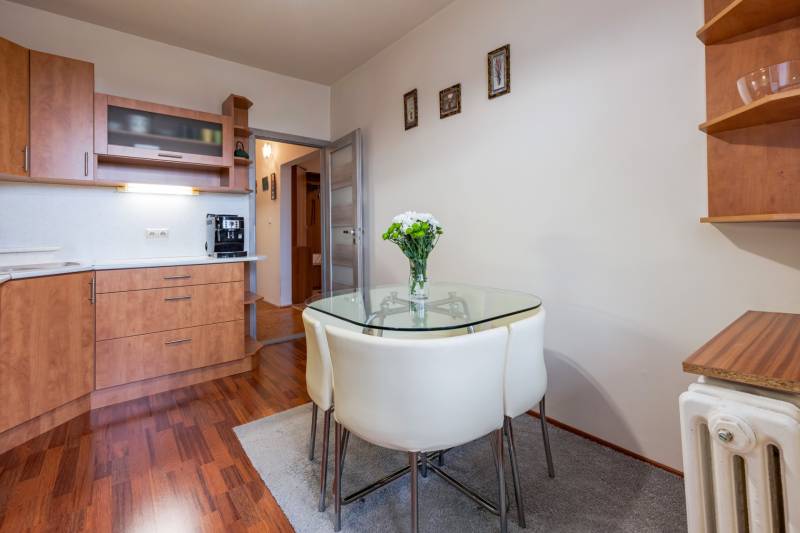 A kitchen in a 4-room apartment with a glass table, wooden decor flooring, white walls.