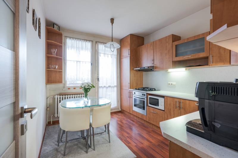 A kitchen in a 4-room apartment with a wooden decor floor, a dining table, and appliances.
