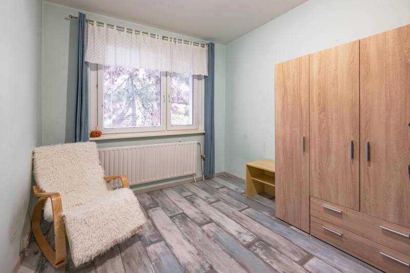 A room in a 4-room apartment with a wardrobe, an armchair, and a floor with a wooden decor.