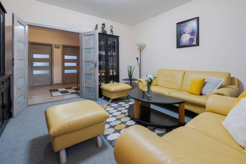 Living room of a 4-room apartment with a yellow leather sofa, glass display cabinet, and a painting on the wall.