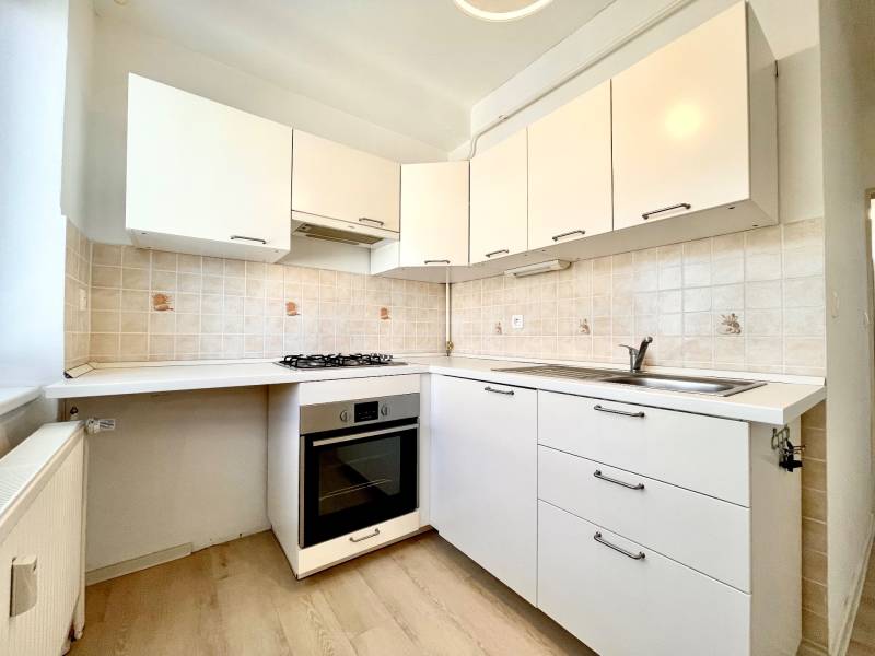 A kitchen in a studio apartment with white cabinets and a wooden decor floor.