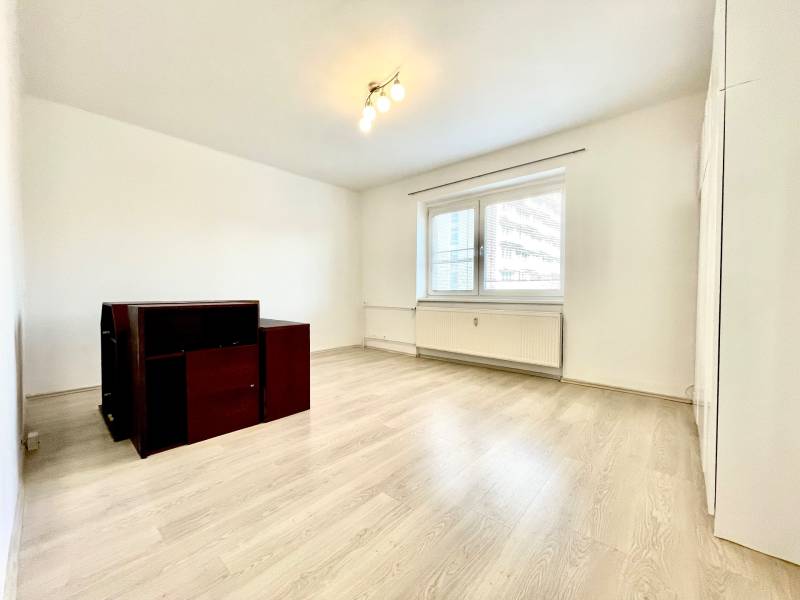 A room with a wooden decor floor and simple furniture in a studio apartment.