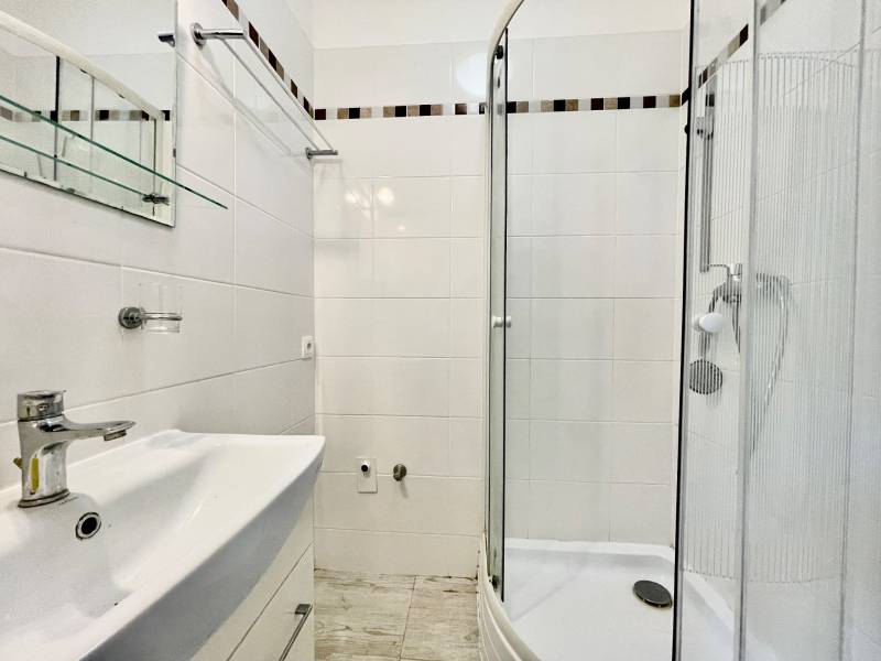 Bathroom in a studio apartment with a sink and a shower, white tiles.