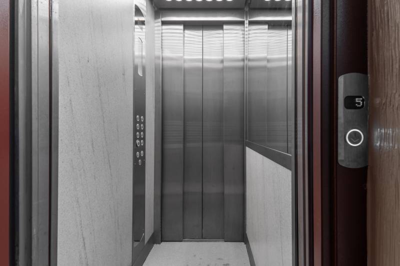 Šedý výťah s kovovou kabínou a ovládacím panelom.