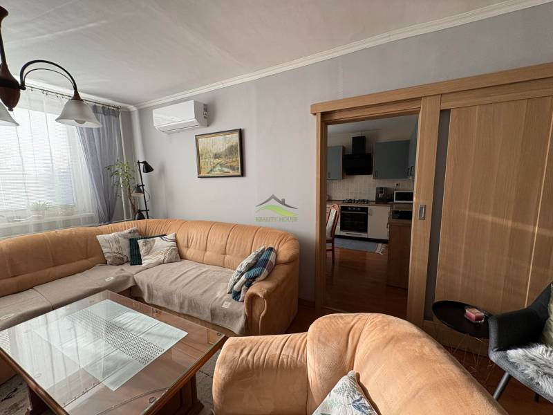 Living room with a sofa, glass table, and kitchen in a three-room apartment.