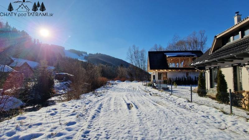 A snowy road in front of the cottage on the street in Mýto pod Ďumbierom, on a sunny winter day.