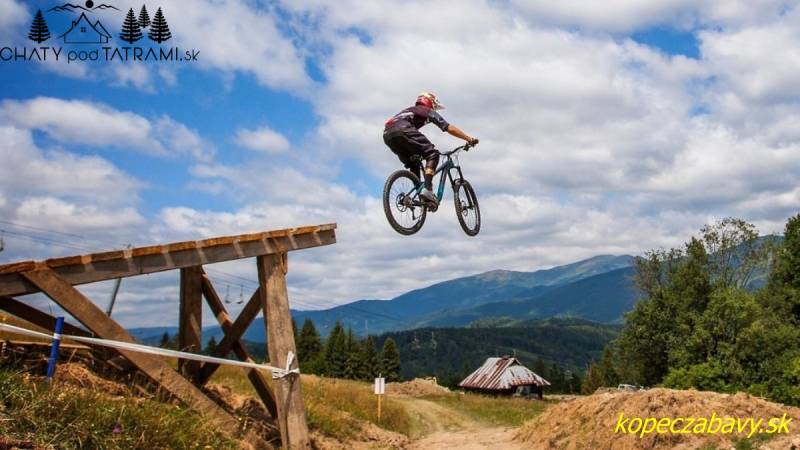 A cyclist is jumping on a track in Bystré, with a view of hills and cottages.