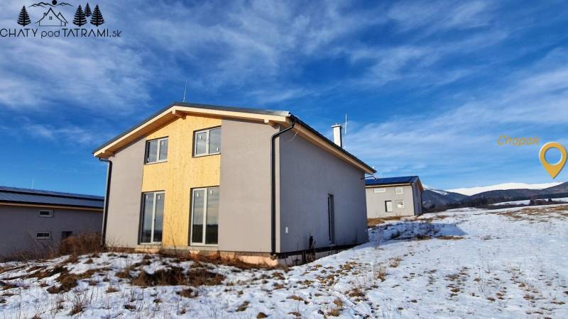 A cottage in Dolná Lehota with wooden cladding, a snowy landscape, and mountains on the horizon.