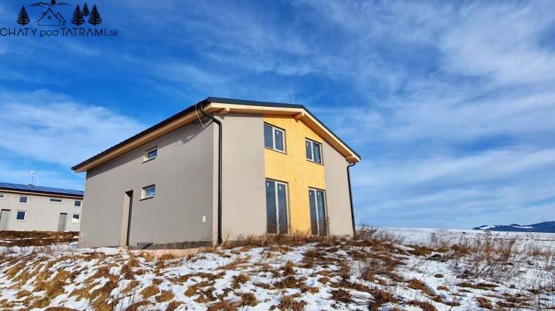A cottage in Dolná Lehota with wooden decor, a snowy plot, and a cloudy sky.