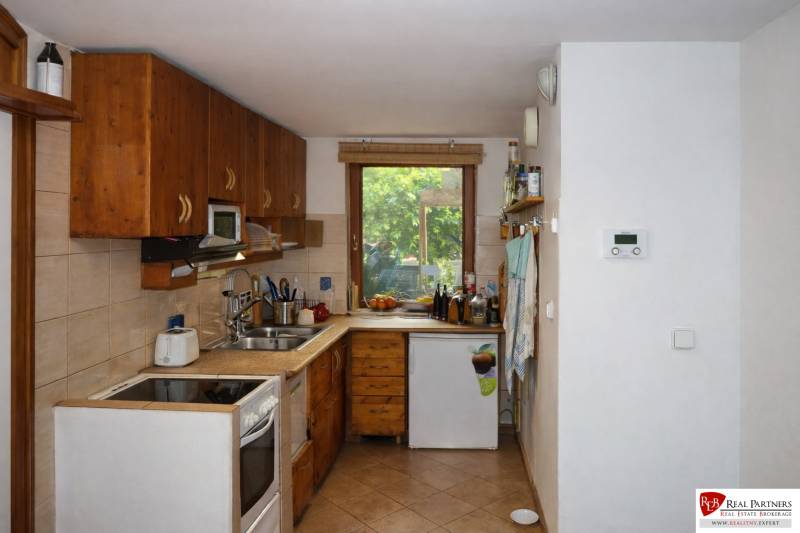 A kitchen in a 3-room apartment with wooden decor cabinets and a window overlooking the garden.