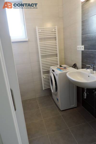 A small bathroom contains a washing machine, a sink, and a radiator, on Bodona Street in a studio apartment.