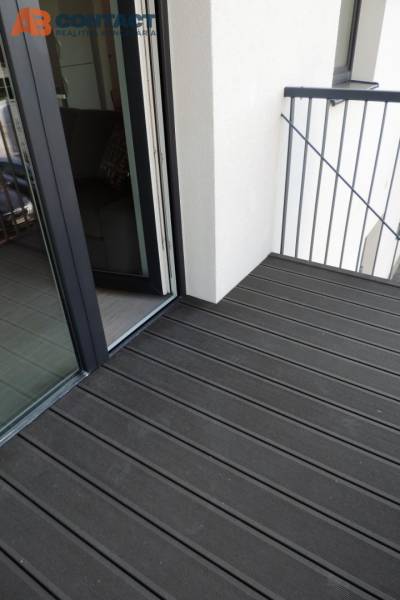 A balcony with a wooden floor on Bodona Street, part of a studio apartment with a large window.