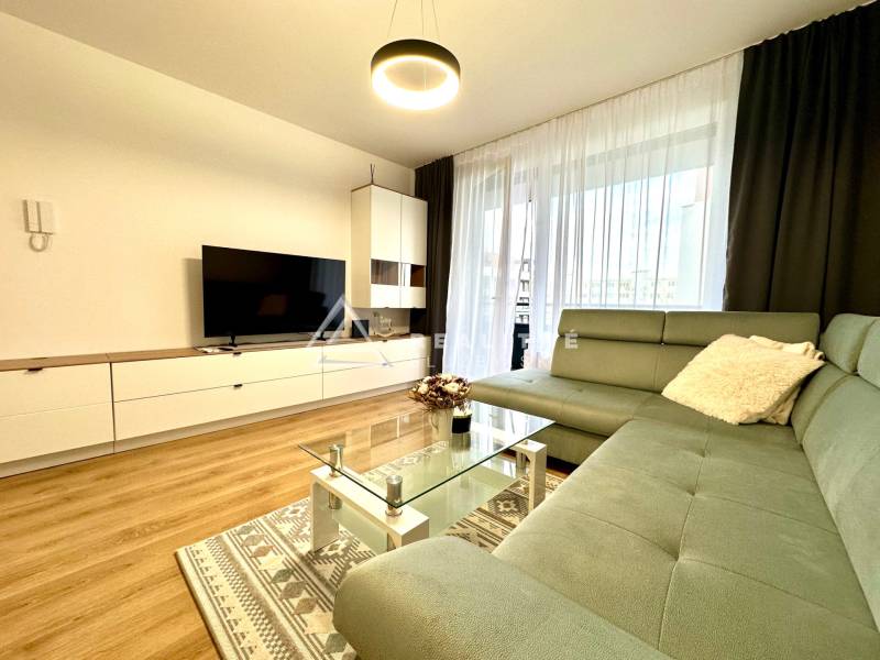 Living room in a two-room apartment with a sofa, television, and wooden decor flooring.