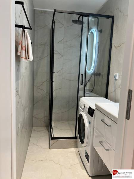 Bathroom in a 2-room apartment with a sink, shower, and washing machine in white design.