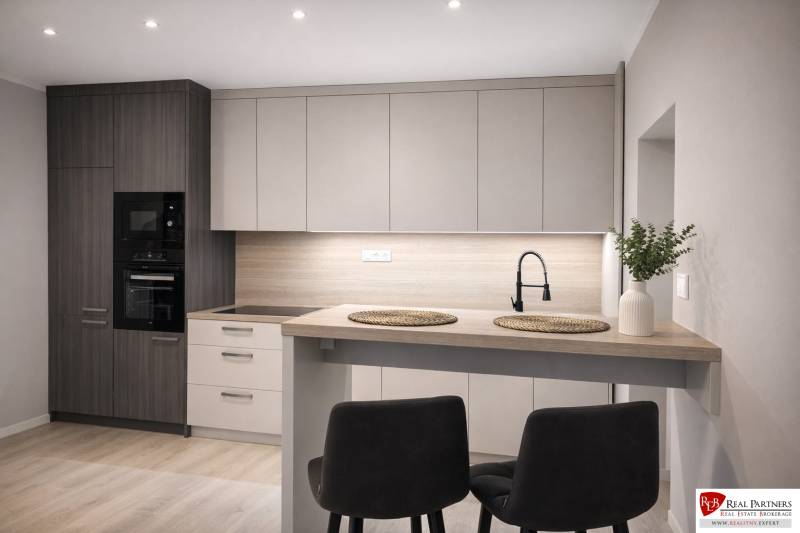 A kitchen in a 2-room apartment with a wooden decor floor, a modern kitchen unit, and a dining table.
