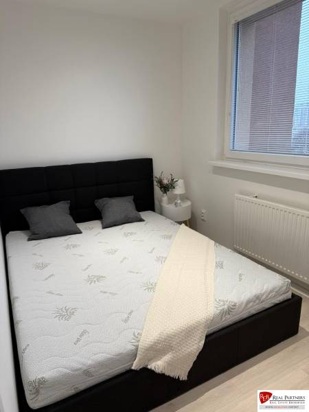 Bedroom in a 2-room apartment with a black headboard, white bedspread, and window with blinds.