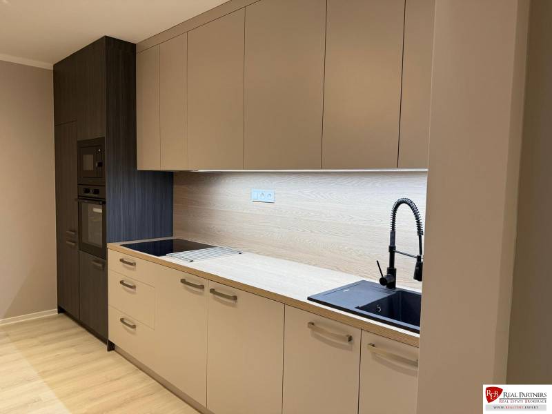 A kitchen unit in a 2-room apartment with a wooden decor floor and built-in appliances.