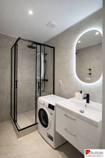 Bathroom in a 2-room apartment with a washing machine, shower cabin, and illuminated mirror.