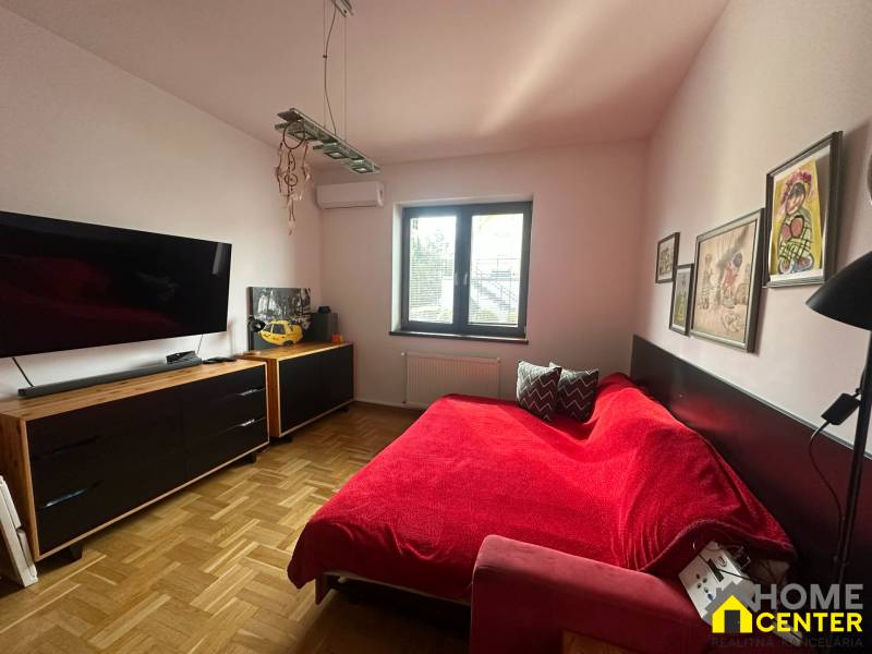 A bedroom in a family house with a red sofa, artworks, and a wooden decor floor.