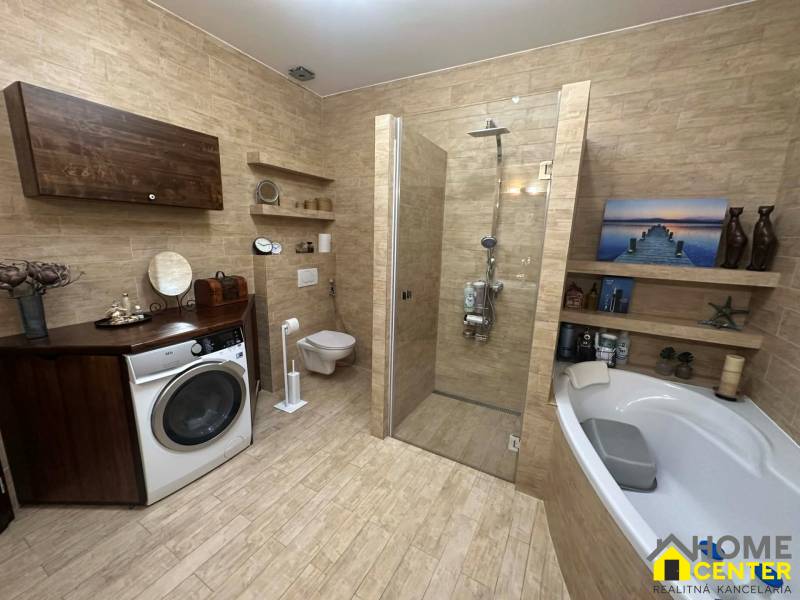 A family house bathroom with a washing machine, bathtub, and shower, floor with wooden decor.