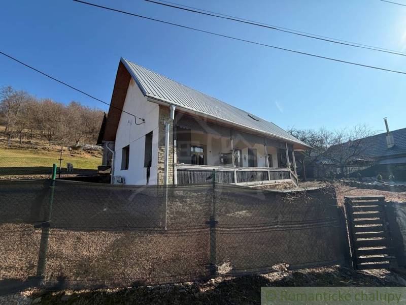 A family house in Ratkovské Bystré with a sloped plot, a metal roof, and a wooden fence.