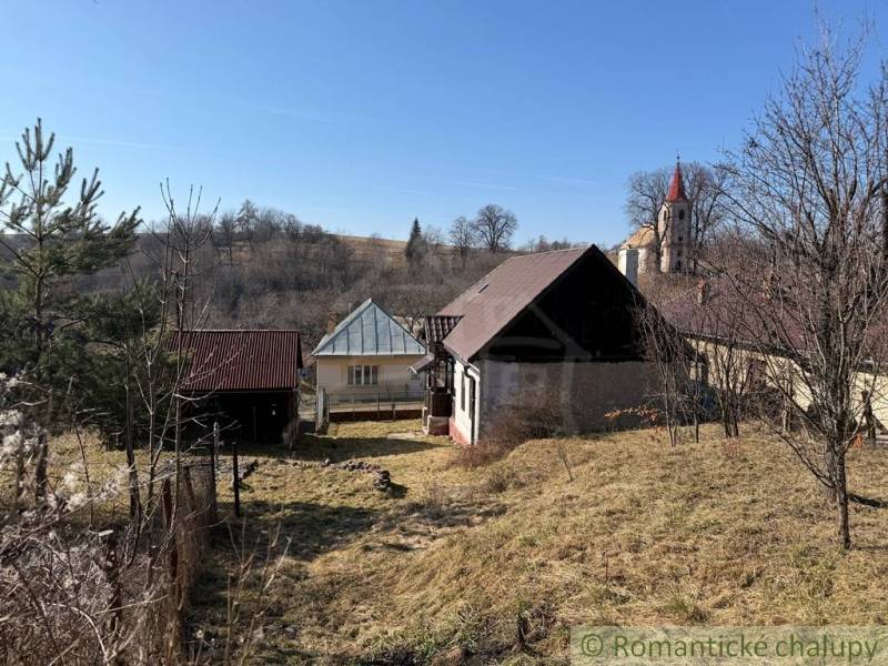 A family house in Lipovec with a church tower in the background surrounded by hilly countryside.