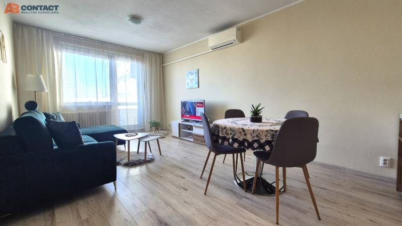 Living room in a two-room apartment with a wooden decor floor, a sofa, and a dining table.