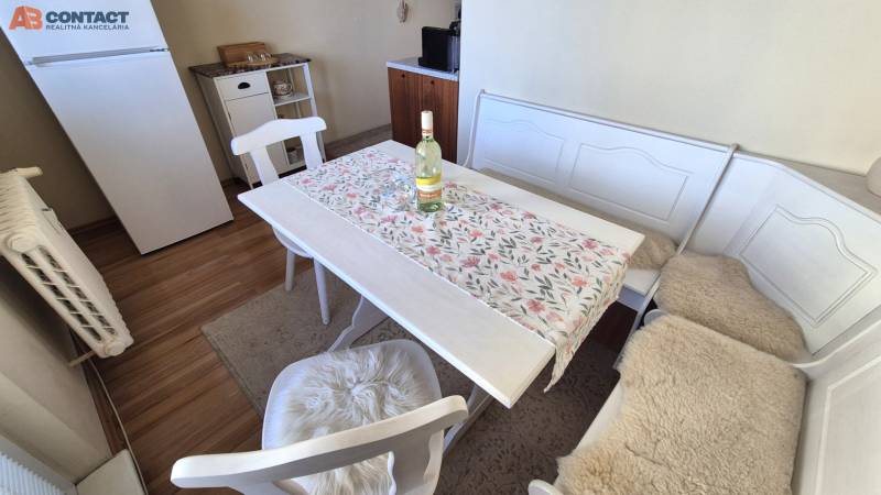 Dining area with white furniture, a refrigerator, and a wooden decor floor in a 2-room apartment.