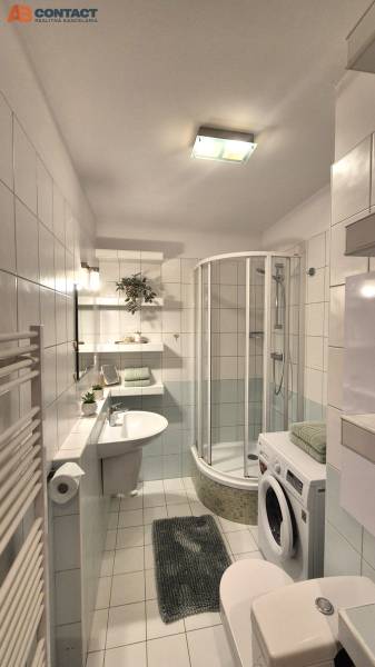 Bathroom in a 2-room apartment with white tiles, a shower, and a washing machine.