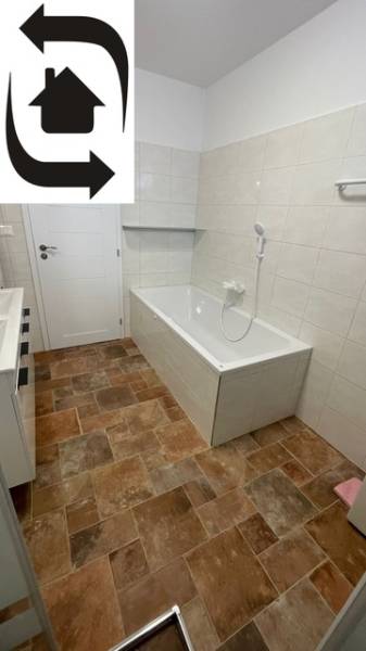 The bathroom in the family house has a bathtub, white tiles, and a floor with a wooden decor.