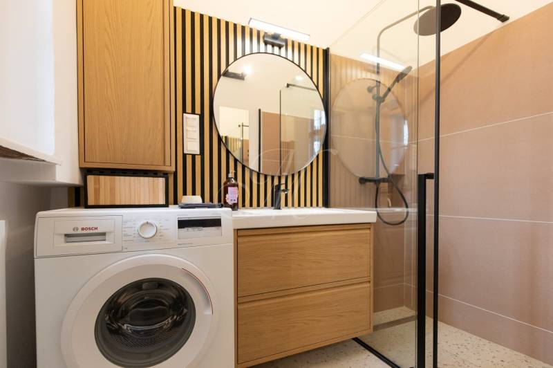 Bathroom with a washing machine, sink, mirror, and shower in a 3-room apartment.