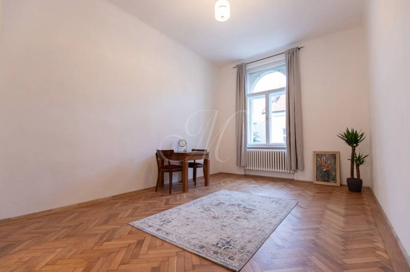 A room in a 3-room apartment with a wooden decor floor, a table, and a plant.