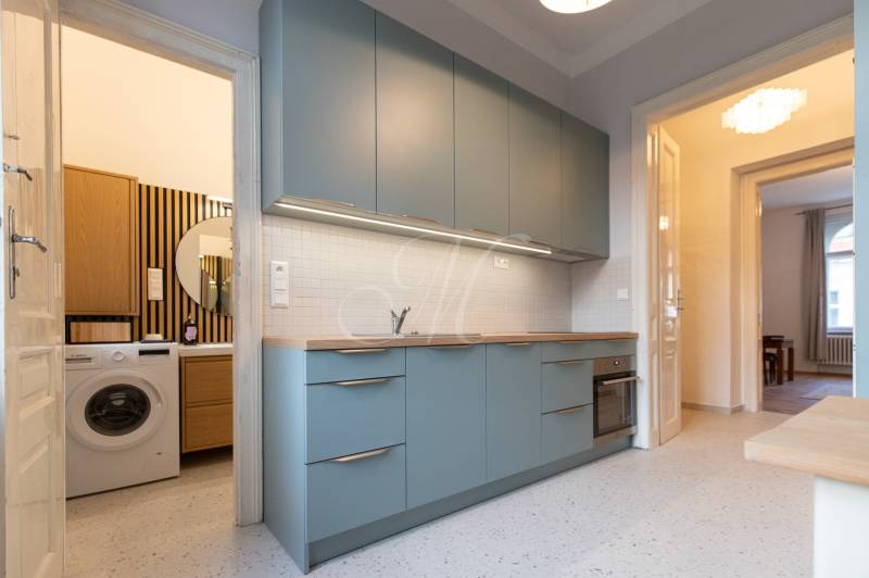 A kitchen with blue cabinets, a sink, and a washing machine in a 3-room apartment inspired by retro style.